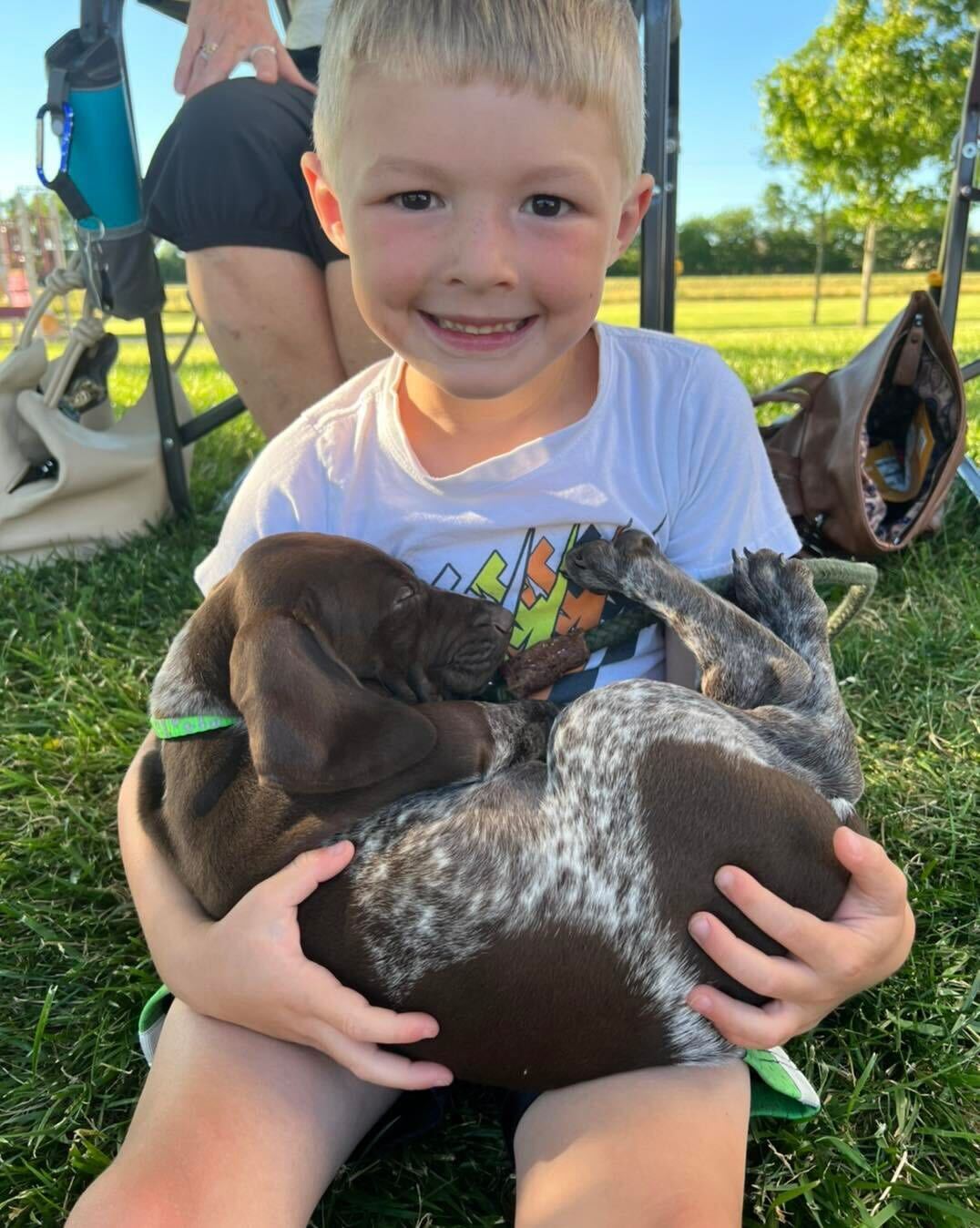 A young boy holds a puppy on his lap outside.